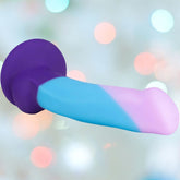 The Avant D16 Purple Haze is a 6.5" slim dildo made from body-safe, non-porous silicone, featuring a purple base merging into light blue and pink on the shaft, set against a softly blurred pastel bokeh background.